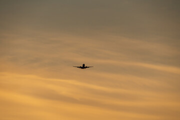 Silhouette of a commercial passenger airplane flying in a beautiful, warm, golden sky during a picturesque sunset or sunrise.