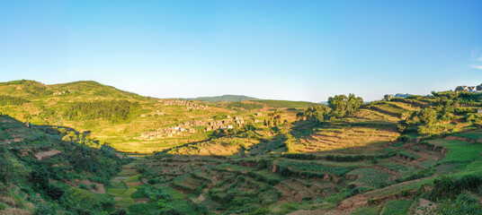 Afternoon sun shines to typical Madagascar landscape in region near Alakamisy Ambohimaha, small hills with terrace fields, clay houses village near
