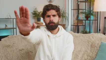 Portrait of Indian young man guy on sofa couch with serious expression doing stop gesture with hand at home, warning of finish, prohibited access, declining communication, and body language danger.