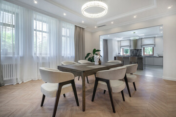 A spacious dining area features a wooden table surrounded by comfortable chairs. Natural light floods the space, highlighting the modern decor and stylish design elements