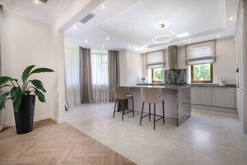 A spacious kitchen features sleek cabinetry, a large island with seating, and abundant natural light from tall windows. The decor is minimalist with warm tones and natural elements