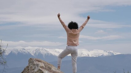 Young hispanic woman standing on a rock with the amazing view of mountain range natural park in the background