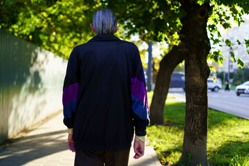 Obraz premium Elderly man walking down a tree-lined street in autumn, enjoying a peaceful afternoon stroll