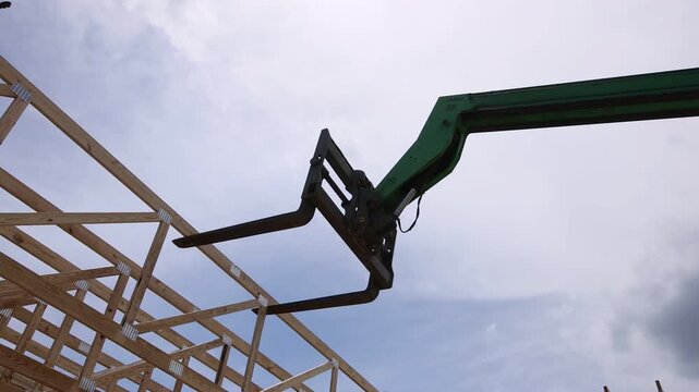 Telehandler maneuvers timber at construction area surrounded by trees on construction site