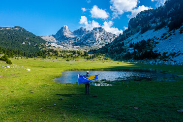Unrecognizable Hiker Holding Bosnian Flag Facing Mountain Peaks and Small Lake in Scenic Landscape