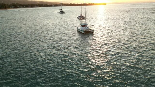 Golden Caribbean sunset over Playa Punta Popy in Las Terrenas. 4K drone footage reveals palm-lined shore, gentle waves, anchored catamarans, and warm tropical light&mdash;ideal for travel, resort, and lifes
