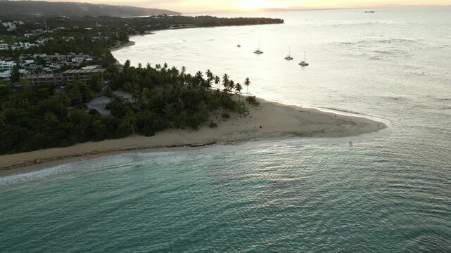 Tropical evening magic above Punta Popy in Las Terrenas. 4K aerial footage shows warm light over palms, quiet surf, and moored catamarans&mdash;great for vacation promos, resort ads, or cinematic B-roll