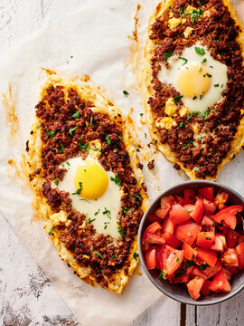 Pide, a tasty Turkish flatbread pizza topped with minced meat and an egg, is set on a wooden table alongside a vibrant salad of fresh tomatoes. Perfect for a communal meal
