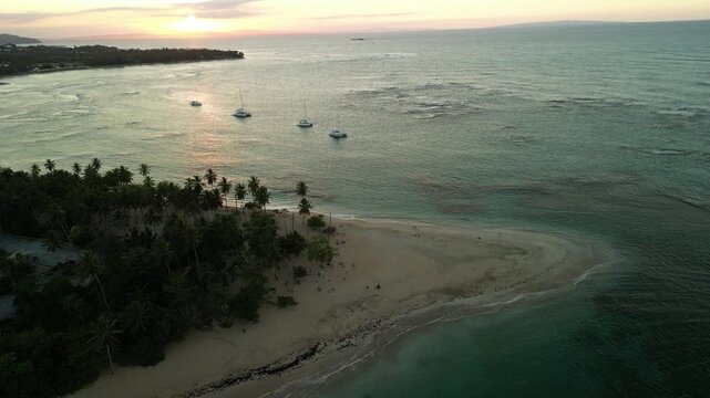 Sunset glows across the Caribbean at Punta Popy Beach. This 4K drone clip highlights a palm-fringed shoreline, gentle sea, and anchored boats&mdash;suited for travel marketing, relaxation content, and luxur