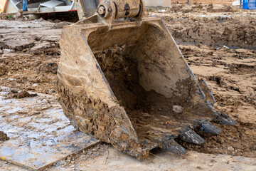 A dirty and muddy excavator bucket lies at a construction site. This heavy equipment is essential for digging and earthmoving on construction and infrastructure projects. © Hafiz