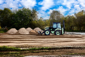 Wheel loader compacts granular surface by repeated passes over soil, creating smooth foundation layer in preparation for future structural installation. © grigvovan