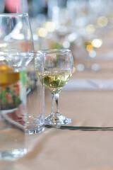 close-up of an elegant glass of white wine and a bottle on a table with a blurred festive setting in the background