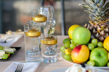 elegant table centerpiece with floating golden candles in glass vases next to a fresh fruit platter including pineapple, apples, and grapes