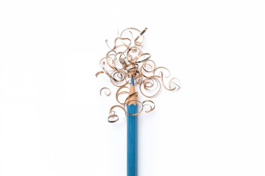 Top view of a sharpened blue wooden pencil with curled shavings on a white surface