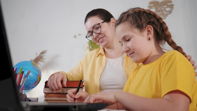 Helping with homework at table mother and daughter tutor with laptop and book for study and education learning together family parent tutor guiding girl through school assignment and practice