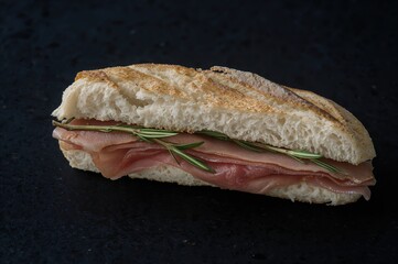 Rustic sandwich with cured ham and herbs against a dark backdrop