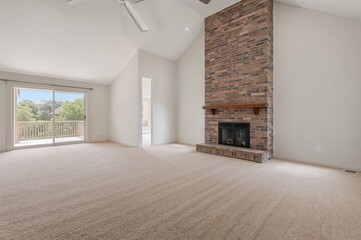 Spacious living area featuring a tall vaulted ceiling and carpeted flooring. Includes a brick fireplace and access to an outdoor deck.