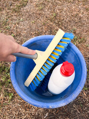 A vertical shot showing a bucket filled with cleaning solution and a brush being held by a hand. 