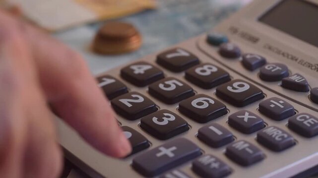 Hand using calculator to do calculations. Concept of rates, interest, billing, and accounts payable. Zoom-in effect.