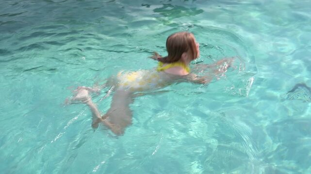 Red-haired girl in yellow swimsuit swimming breaststroke in a blue swimming pool, summer holiday video.	