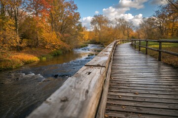 Obraz premium Detailed view of a wooden path bordered by railings alongside a running stream during fall