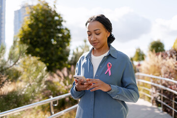 Woman with pink ribbon using smartphone outdoors