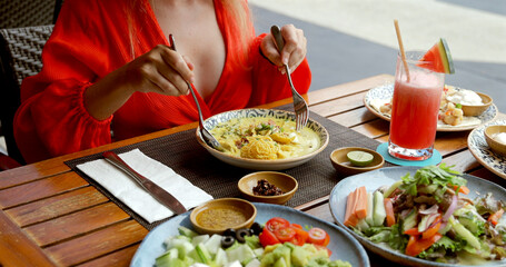 Woman enjoying pasta at outdoor cafe, vibrant salad and fresh watermelon juice on wooden table. Al fresco dining, casual lunch, summer refreshment.