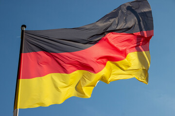 Vibrant flag waving in the wind, showcasing bold colors of black, red, and yellow against a clear blue sky, symbolizing national pride and identity