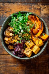 Freshly prepared vegetable bowl features roasted squash, tofu, vibrant greens, and mushrooms. Perfect for a healthy meal, this dish is beautifully arranged in a rustic setting