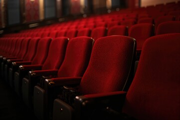 Fototapeta premium Empty vintage red seats in a quiet cinema hall, soft focus close-up of movie theatre seating.