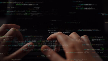 Close-up view of hands typing on a laptop keyboard with abstract programming code in the...