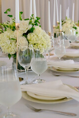 Elegant indoor wedding table setup featuring white roses and hydrangeas, gold candle holders with taper candles