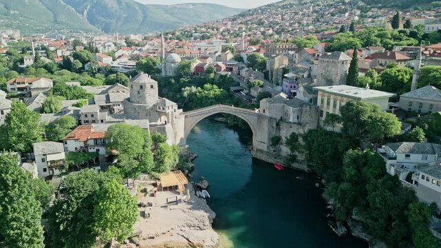 Mostar, Bosnia and Herzegovina Aerial dolly drone video flying along the Neretva River, bypassing the Old Bridge, and centering on Koski Mehmed Pasha Mosque with surrounding old town and hills