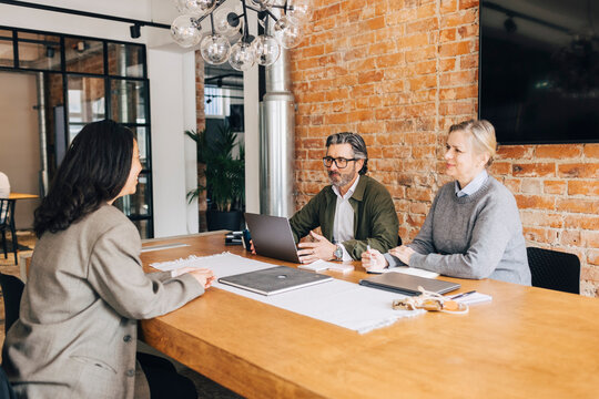 Male and female human resource expert taking interview of woman while sitting at table in office