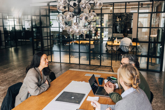 High angle view of smiling female giving interview to business professionals while sitting at table in office