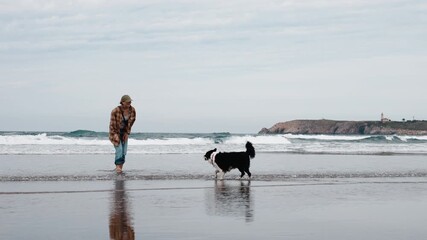 A young woman in a plaid shirt plays with her Border Collie on the ocean shore. Concept joy, friendship between human and pet, freedom in nature.