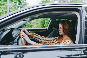 Naklejka premium A woman driver sits in a modern car with hands on the steering wheel, focused on the road as daylight filters through the window.
