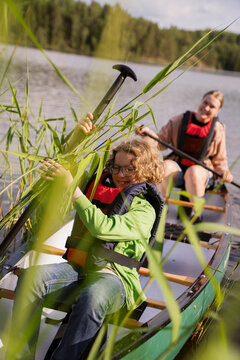 Smiling boy wearing life jacket rowing canoe in lake with female guide at summer camp