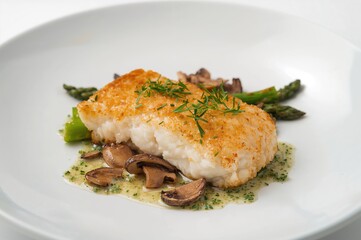 Close-up of a crispy fried fish filet served with green asparagus and mushrooms on a plate