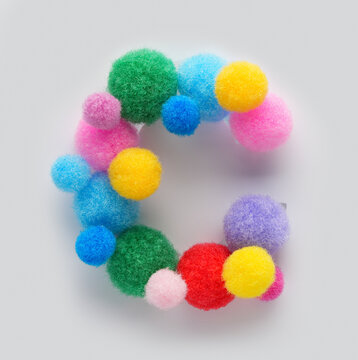Colorful letter C made of fluffy pom poms on white background. Creative handmade typography for kids learning alphabet, educational design, playful classroom decor, and graphic projects.