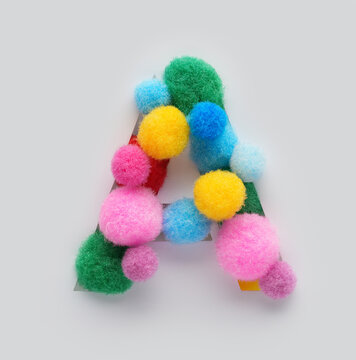 Colorful letter A made of fluffy pom poms on white background. Creative handmade typography for kids learning alphabet, educational design, playful classroom decor, and graphic projects.