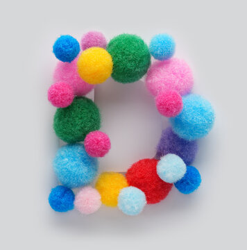 Colorful letter D made of fluffy pom poms on white background. Creative handmade typography for kids learning alphabet, educational design, playful classroom decor, and graphic projects.