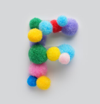 Colorful letter F made of fluffy pom poms on white background. Creative handmade typography for kids learning alphabet, educational design, playful classroom decor, and graphic projects.