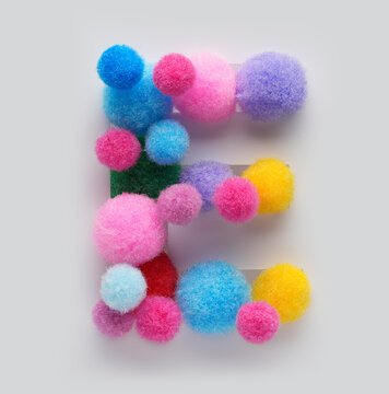Colorful letter E made of fluffy pom poms on white background. Creative handmade typography for kids learning alphabet, educational design, playful classroom decor, and graphic projects.