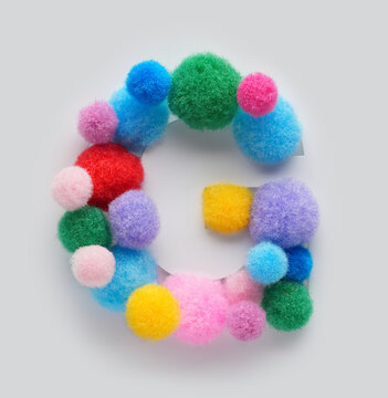 Colorful letter G made of fluffy pom poms on white background. Creative handmade typography for kids learning alphabet, educational design, playful classroom decor, and graphic projects.