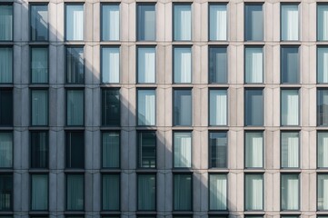 Modern office building with numerous glass windows forming a geometric design on a gray concrete wall, highlighted by sunlight and shadows in a minimalist style