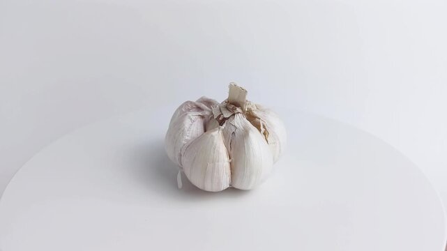 Slow loop of a single garlic bulb rotating on white podium, perfect for cooking, health, spice, and food preparation concepts.
