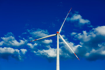 Captivating wind turbine stands tall against a vibrant blue sky filled with fluffy clouds in a serene landscape © DSMT