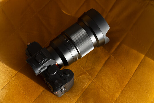 Professional black mirrorless digital camera with a large zoom lens resting on a textured, golden-yellow velvet sofa.