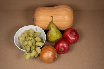 Autumn Harvest: Butternut Squash, Pear, Grapes, and Pomegranates on Brown Background